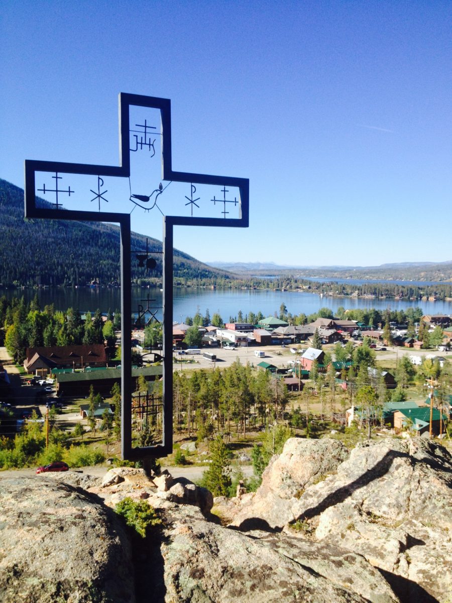 Cross on hill with mountain lakes in background.