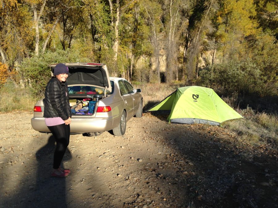 Girl smiling in the cold next to car with open trunk.