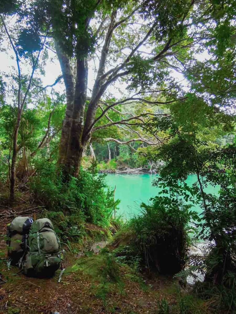 Two backpacks on ground next to glacier fed river.