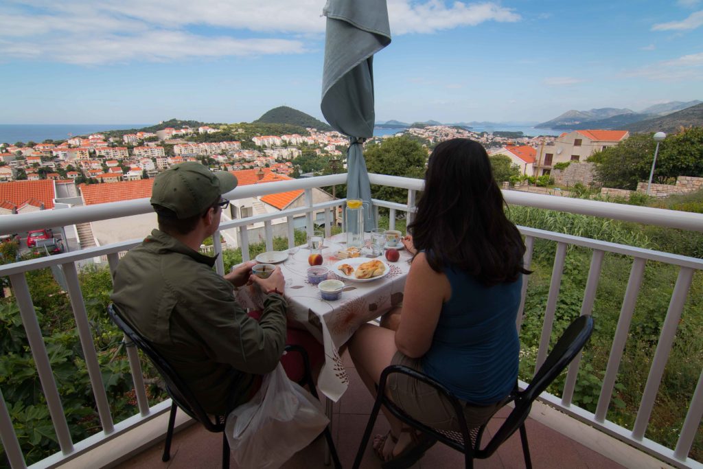 couple sitting at table with breakfast overlooking a town with ocean in the distance.