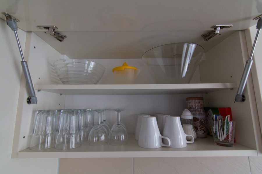 cupboard open with medium and large bowl on top with lemon squeezer in between. On bottom shelf clear cups and white coffee mugs