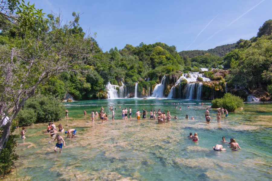 Krka Waterfalls with people swimming in the water below the waterfall.