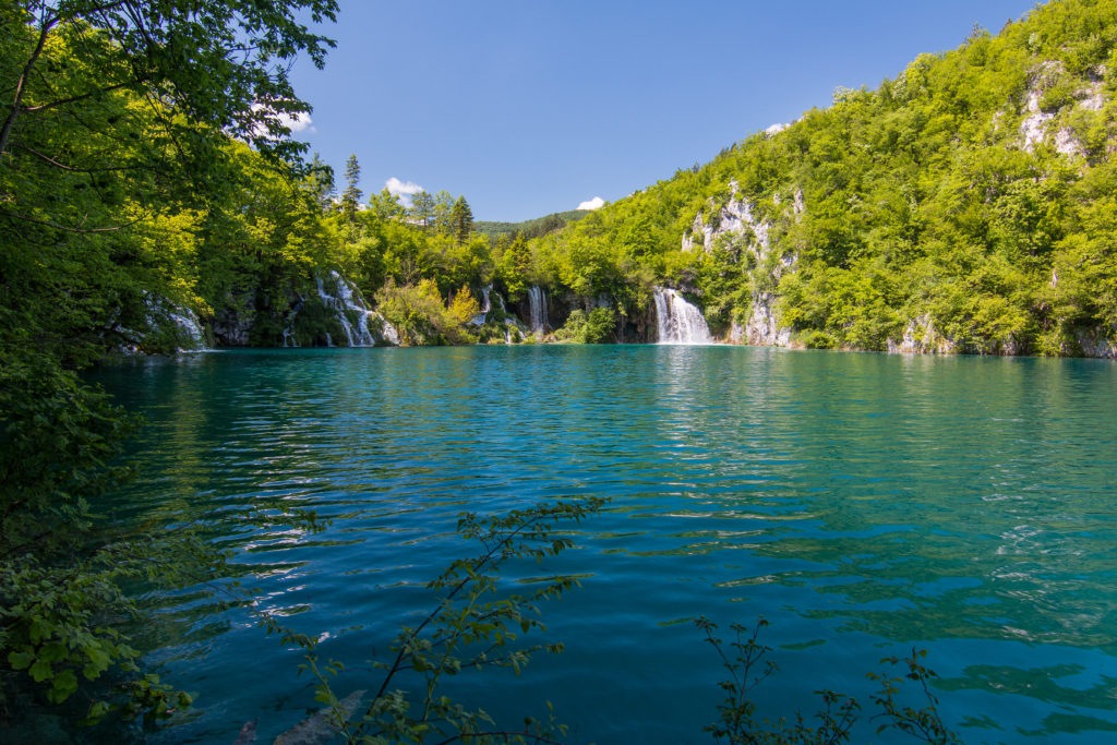 turquoise waters with lush green vegetation around and waterfalls coming through the greenery