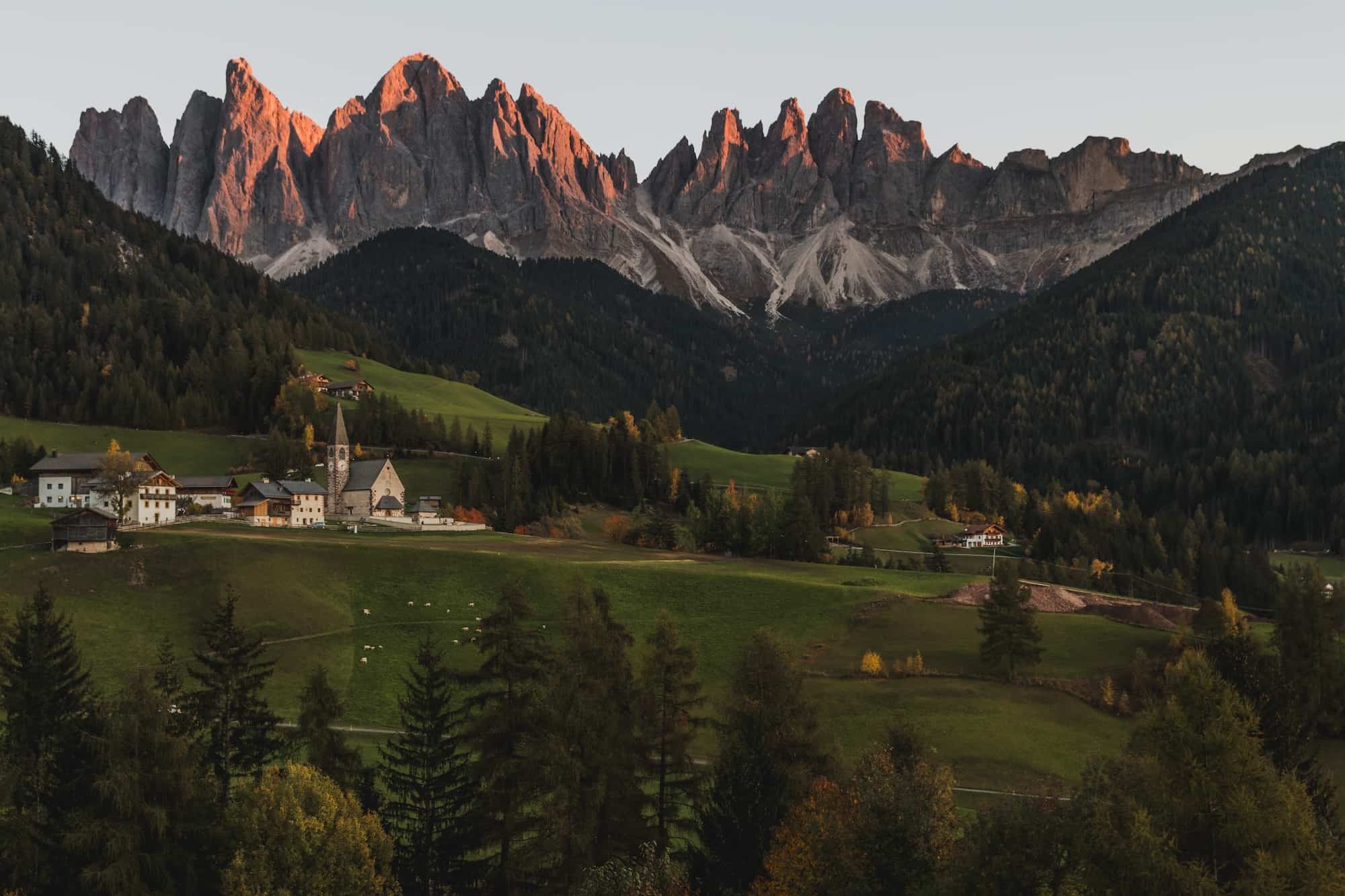 Italian cathedral church with mountain peaks in background at sunset.