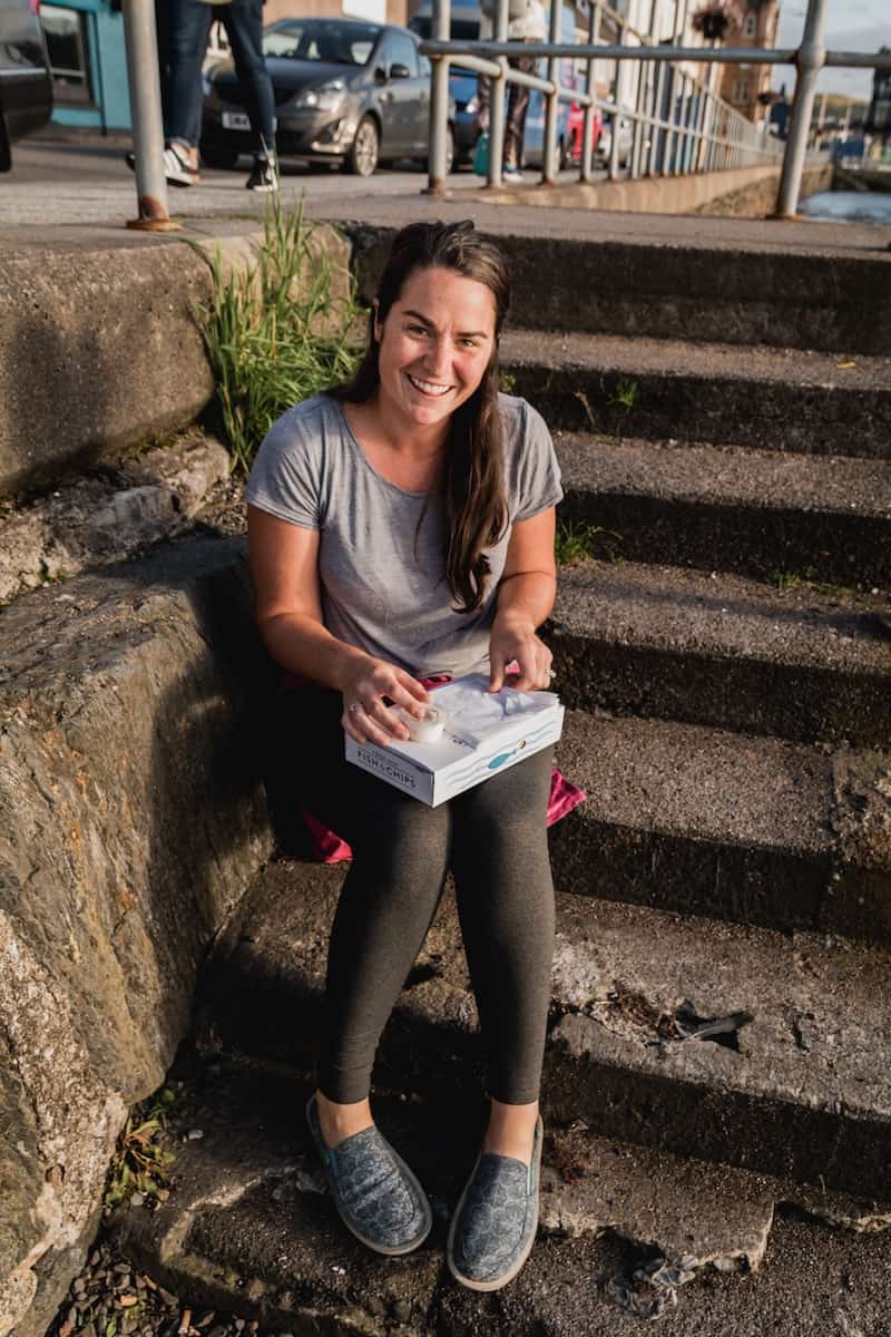 Woman sitting on stairs holding to-go box.