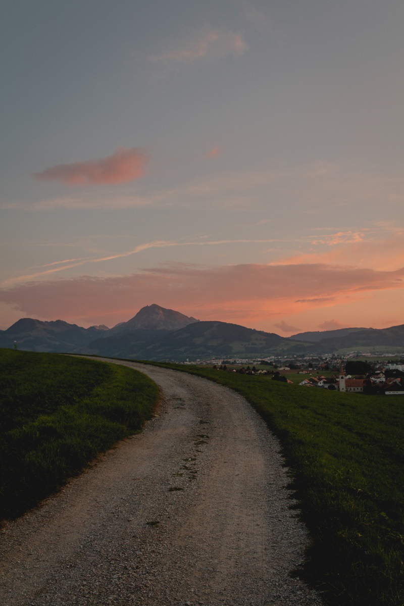 A back country road in Switzerland at sunset with mountain peaks.
