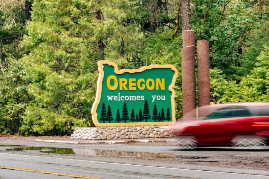 Motion blur of red car driving past green Welcome to Oregon sign.