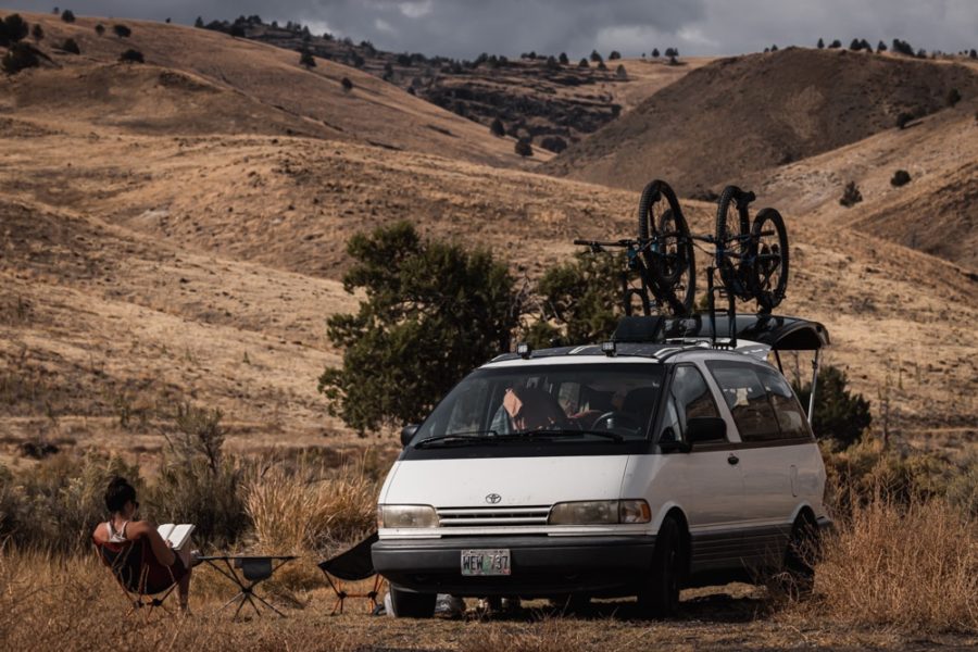 woman reading book in camp chairs next to campervan with rolling hills in background, ArboursAbroad, Oregon