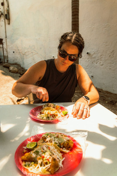 A woman squeezing lime on a plate of fish tacos at a table in the shade in Puerto Vallarta.