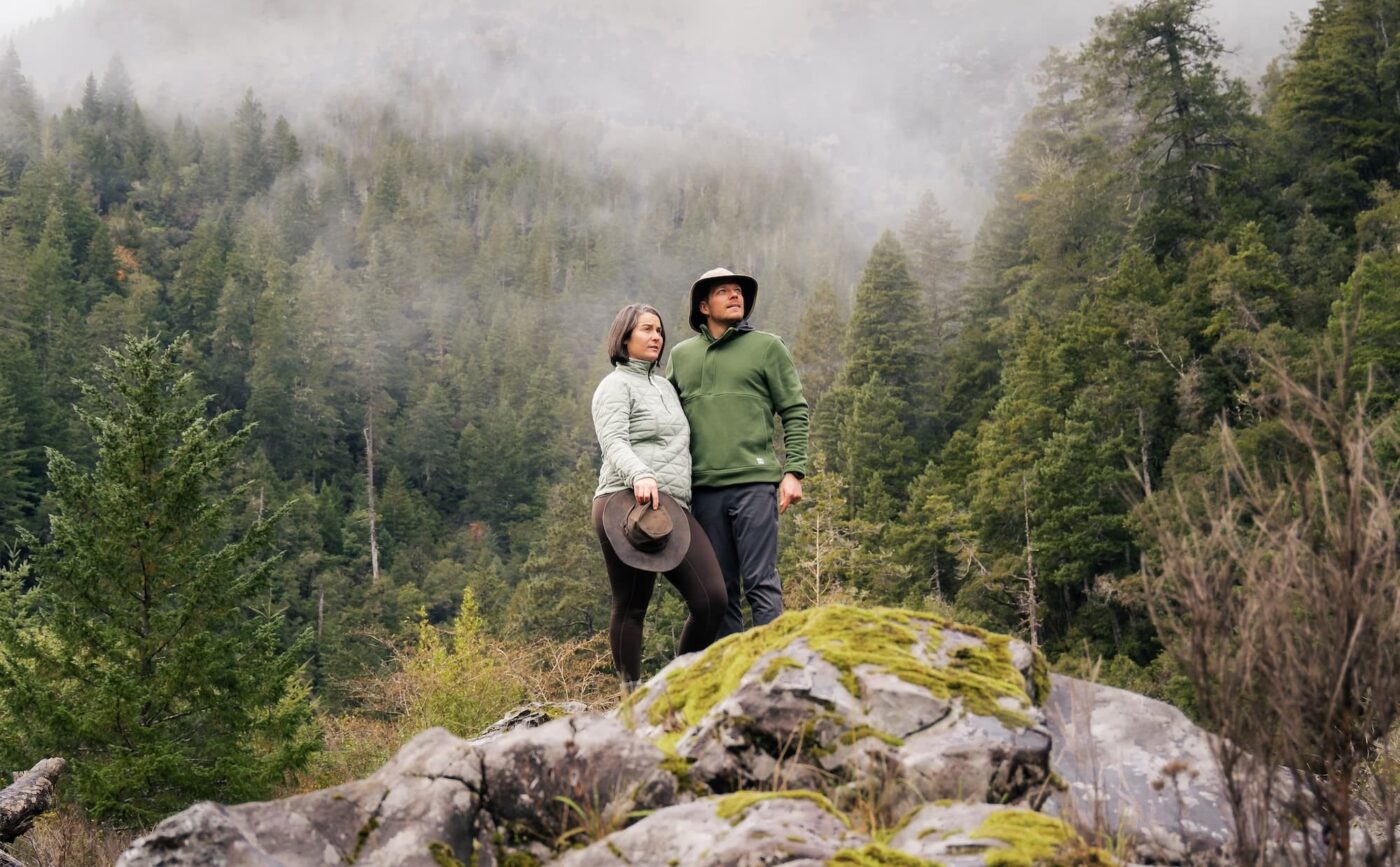 Young couple standing on rock in forest looking into distance and holding each other.