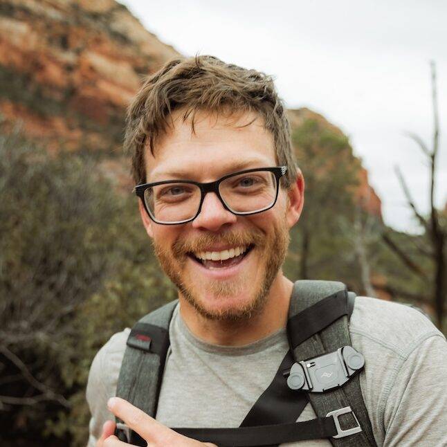 Young man smiling at camera with backpack on in the red rock desert.