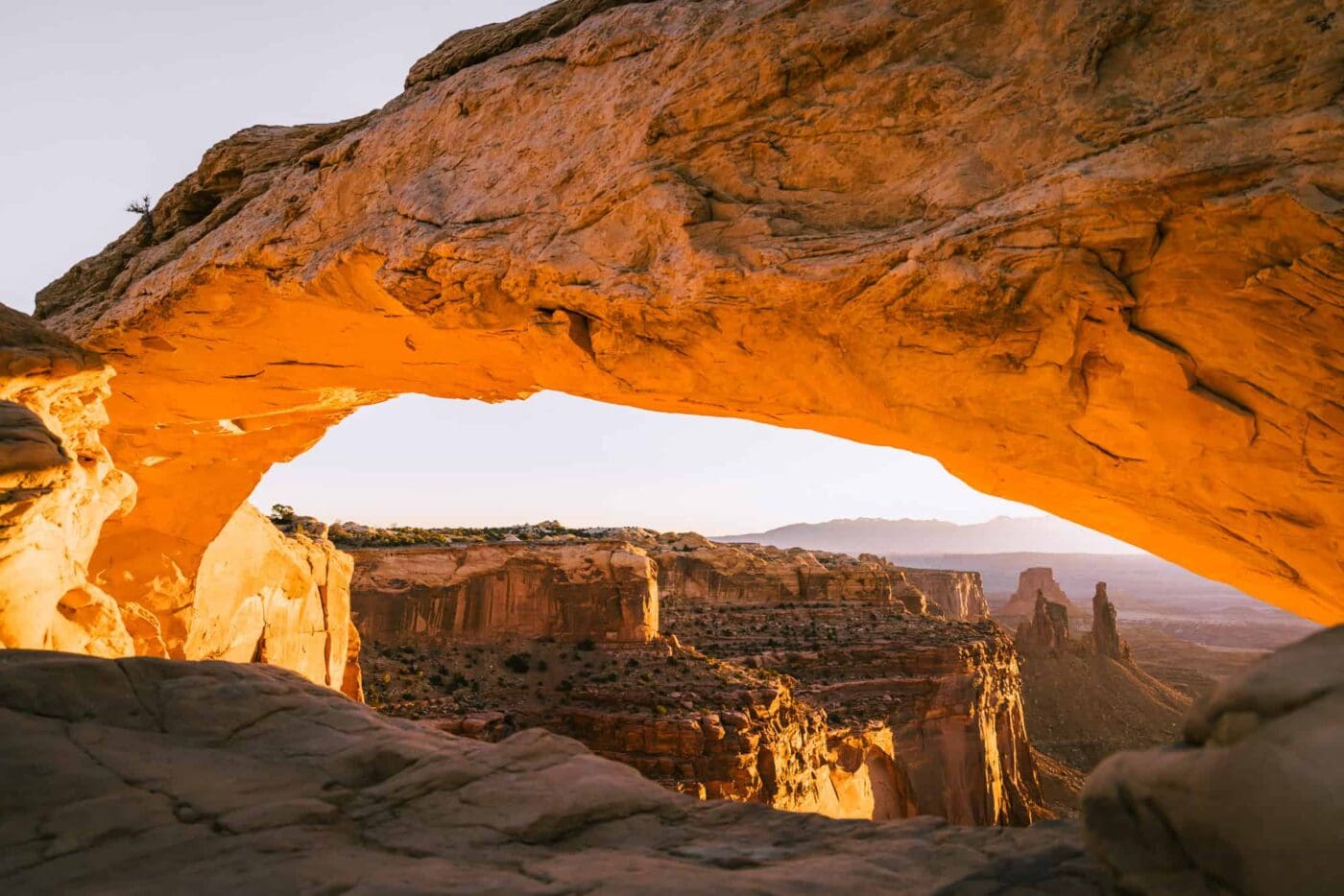 orange of sunrise illuminating a rock arch in the desert.