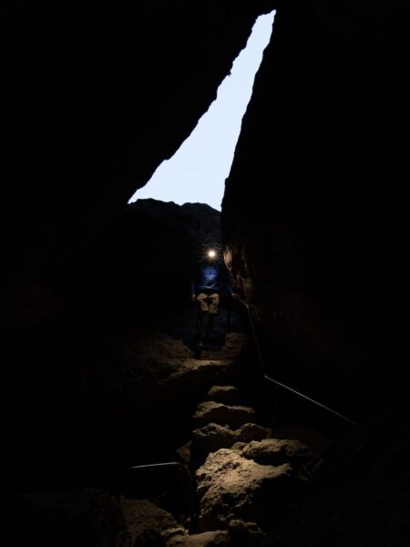 Man walks in cave with headlamp on down stairs.