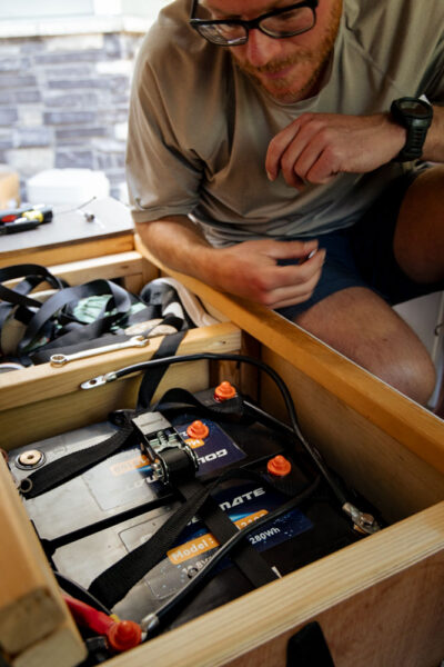 man looking down at two lithium iron phosphate batteries after freshly installing batteries in a self converted minivan.