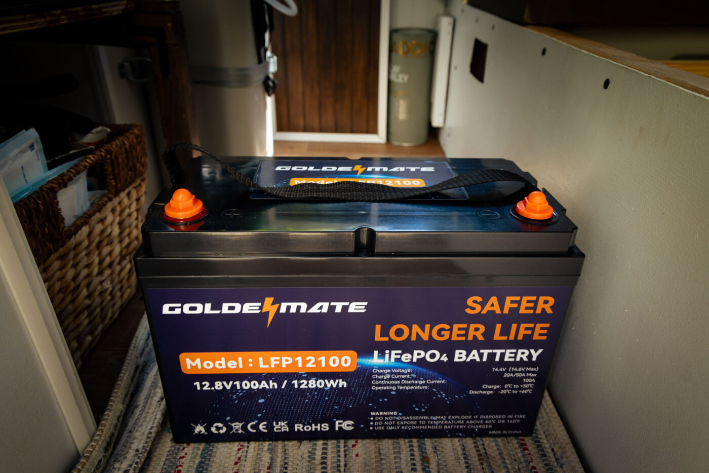 12v 100am LiFePO4 battery by Goldenmate sitting on the van floor of our self converted minivan. Set as arboursabroad hero image.