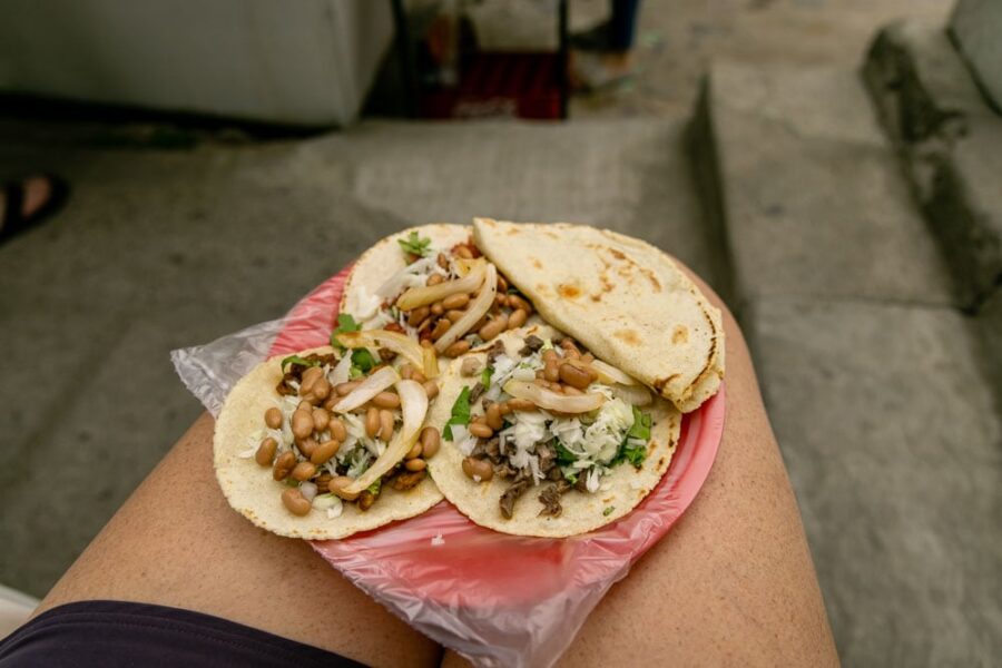 A plate of tacos sitting on women's legs with an extra tortilla on the side.