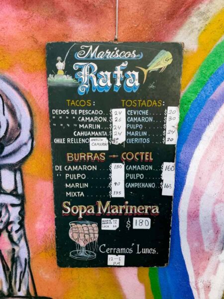 A chalkboard style sign for Mariscos Rafa fish taco stand with their prices and what they offer for food.