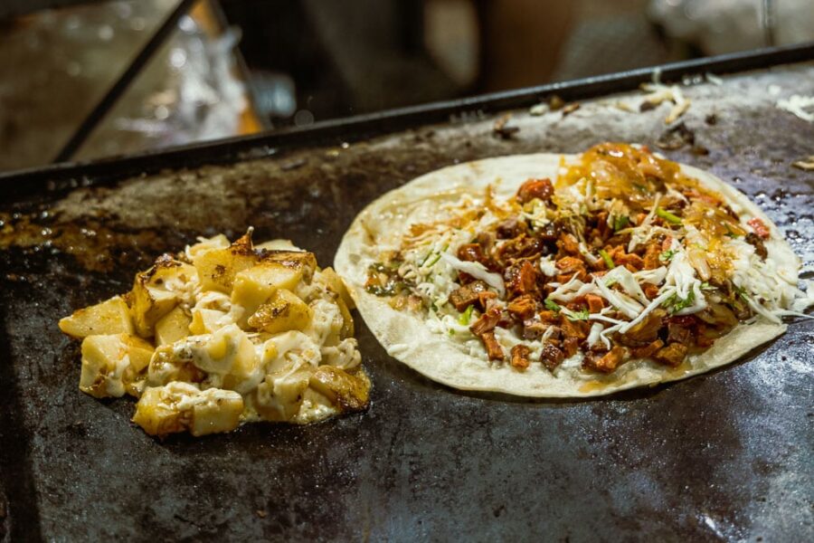 Potatoes and cheese next to a quesadilla with meat and veg on a large skillet.