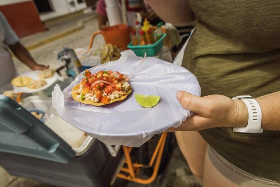 A woman holding a purple plate wrapped in plastic bag with a ceviche tostada and lime on the plate.