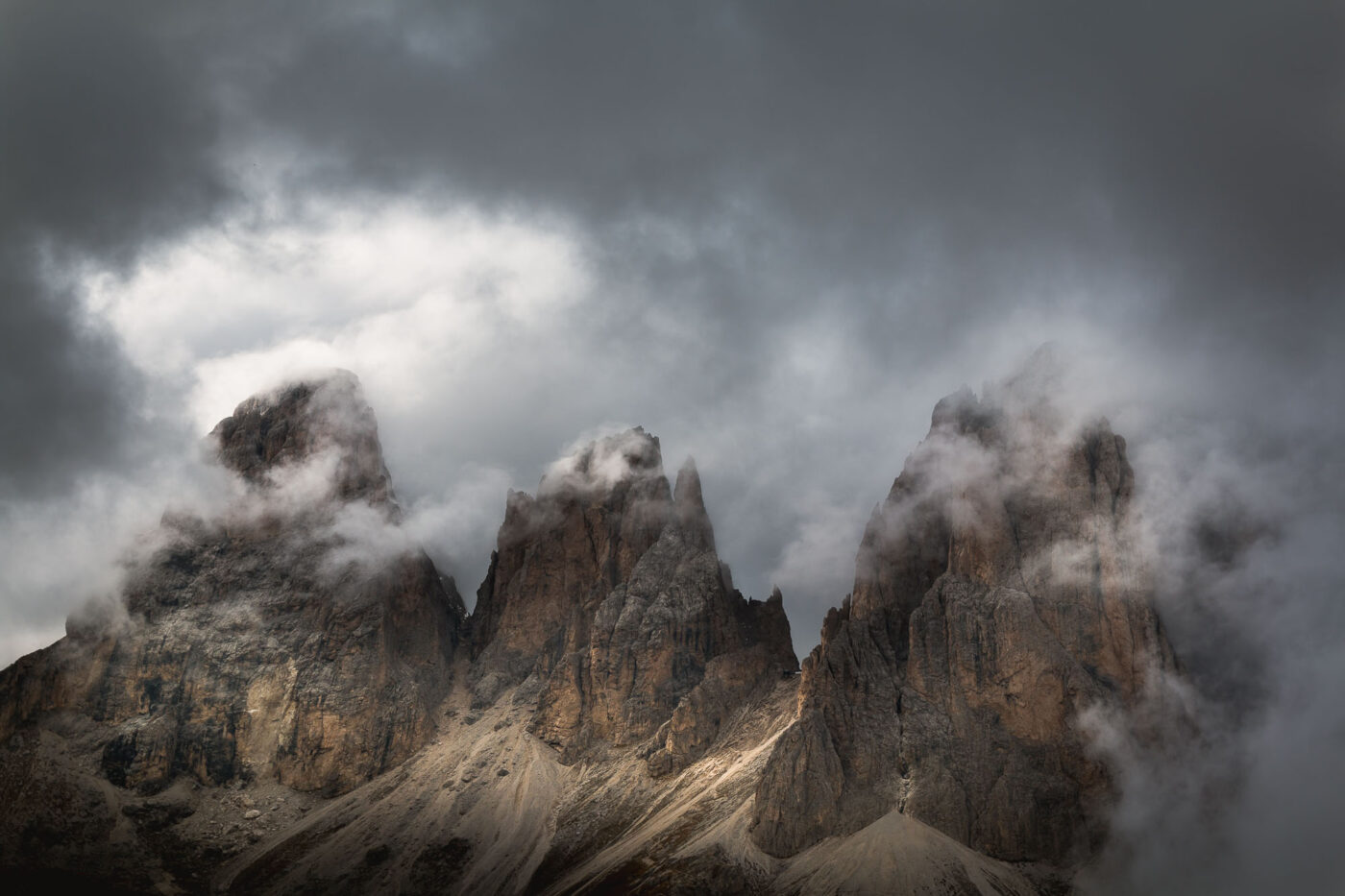Three mountain peaks with clouds surrounding them on a dramatic morning in the Italian Dolomites.