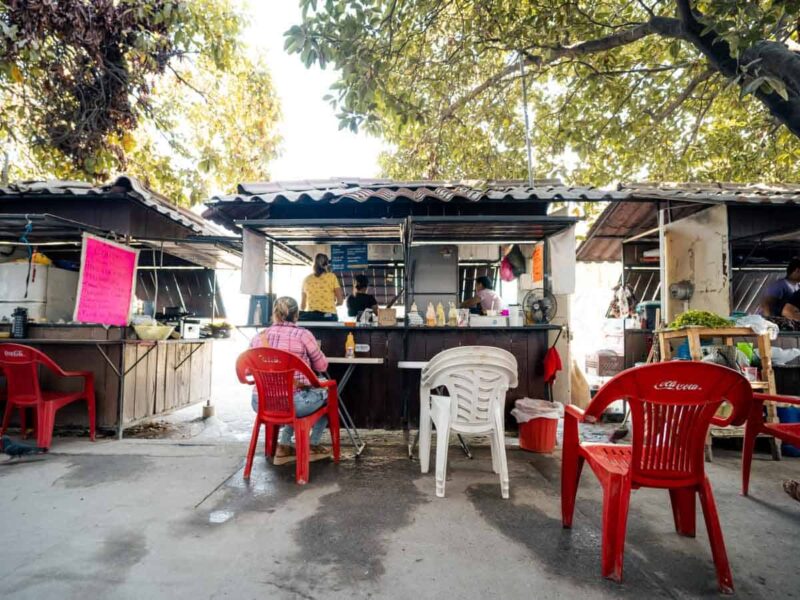 Three taco stands in a row with red and white plastic chairs out front.