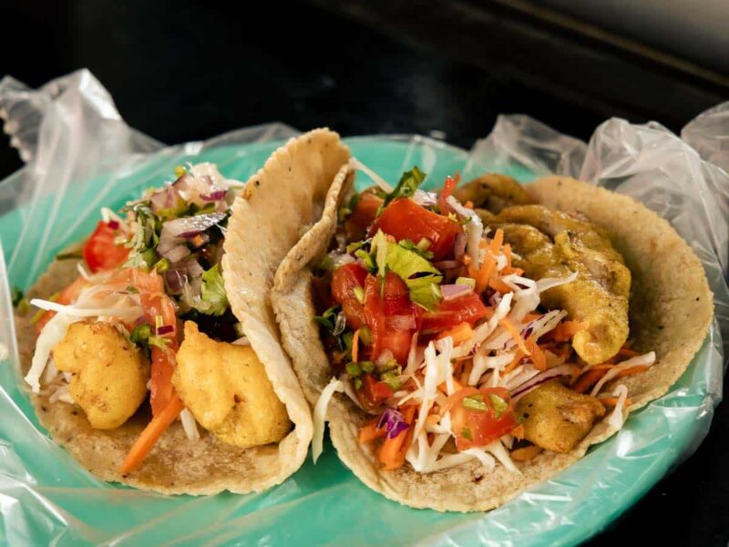 Two fish tacos with shredded cabbage, pico de galo, and green sauce on a teal plate in Puerto Vallarta, Mexico.