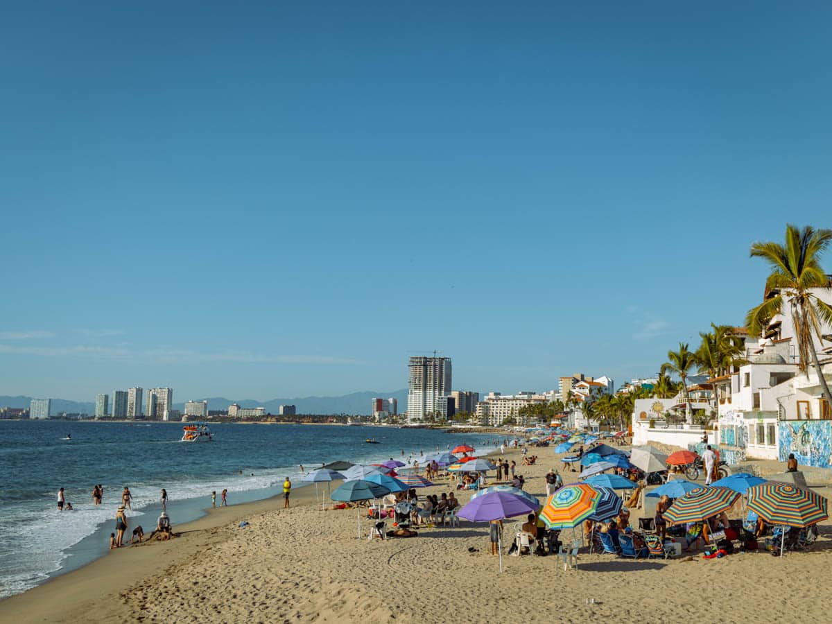 Lots of umbrellas set up on Playa Camerones in Puerto Vallarta on a blue sky day.