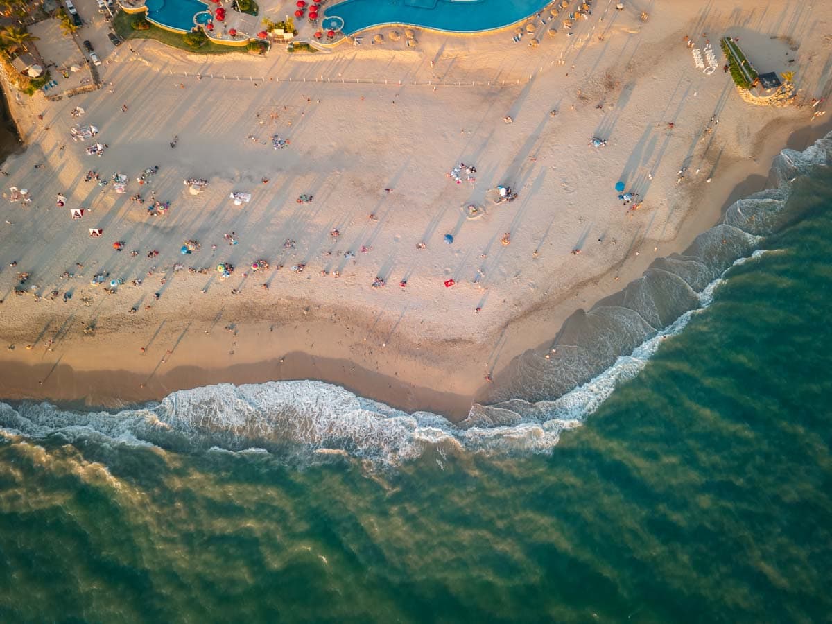 A sandy beach with people set up and the waves crashing in, taken from a drone, shot top down.