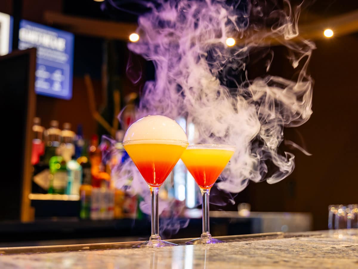 Red and yellow drinks in martini glasses at the Lost Cactus Bar in Las Vegas with smoke billowing around them.