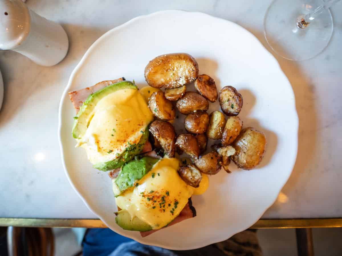 Eggs Benedict with potatoes on a white plate.