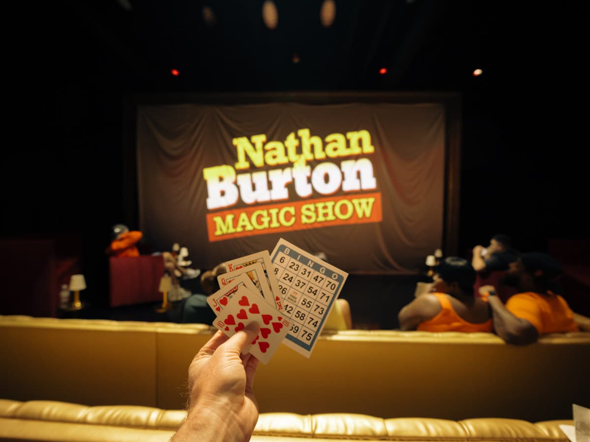 The Nathan Burton Magic Show on a projector screen with hand holding cards and a bingo card.