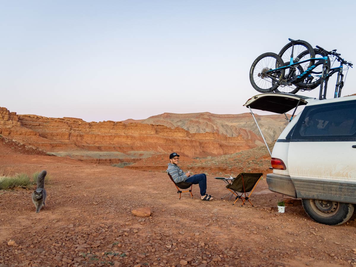 Jason from ArboursAbroad with cat, Georgie, sitting behind the van with back of van open and iconic red rock cliiffs behind.