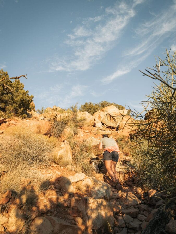 Heather hiking up a rock scramble in Sedona with blue skies behind her.