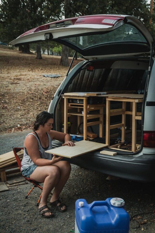 Woman sitting in a chair trying to figure out the back of her camper van build fold out table.