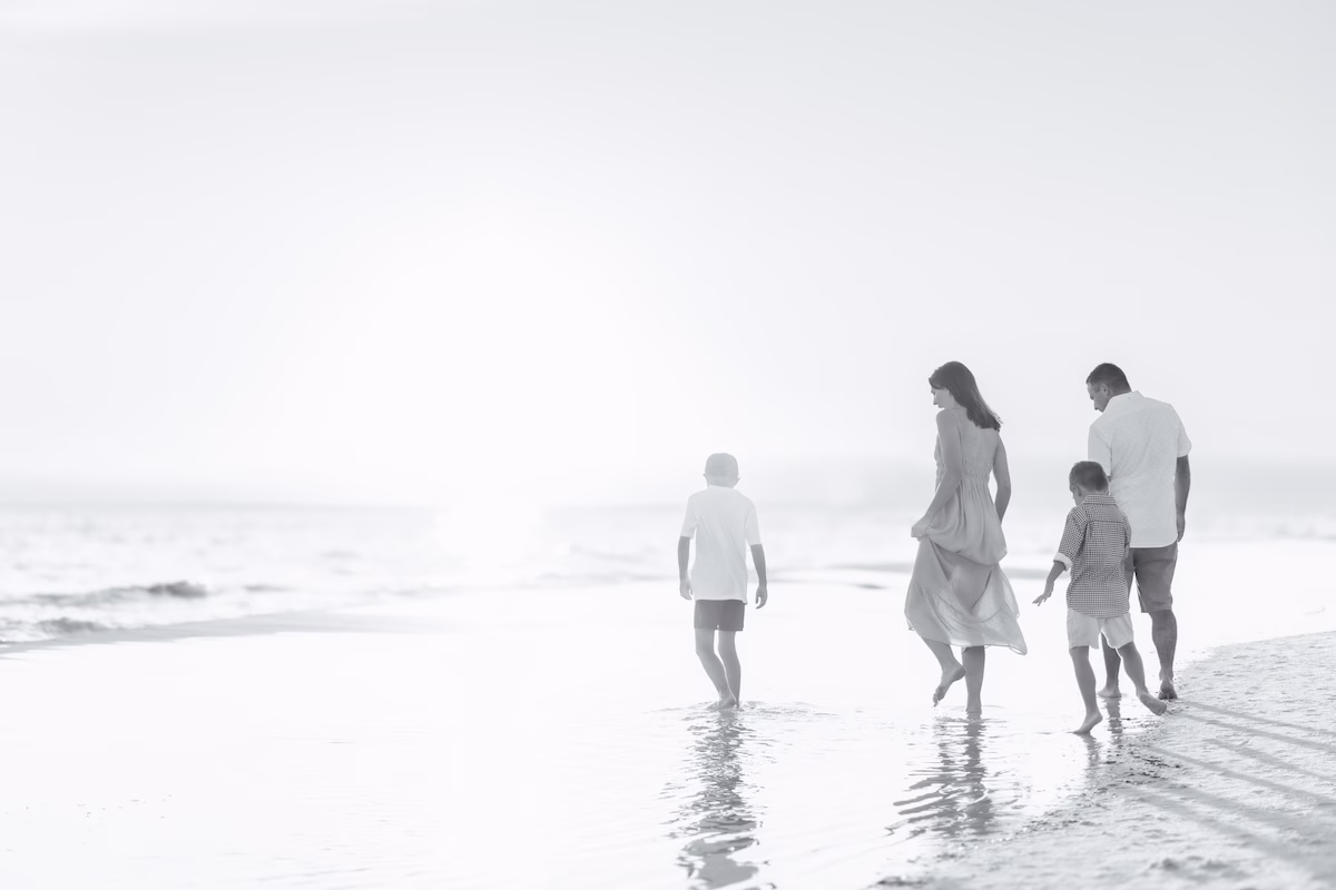 Family of four walking on beach at sunset in a black and white edit.