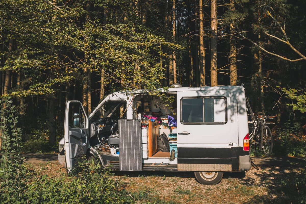 Small wheel base sprinter van, low roof, with inside built out and solar panel hanging between the open front and slider door.