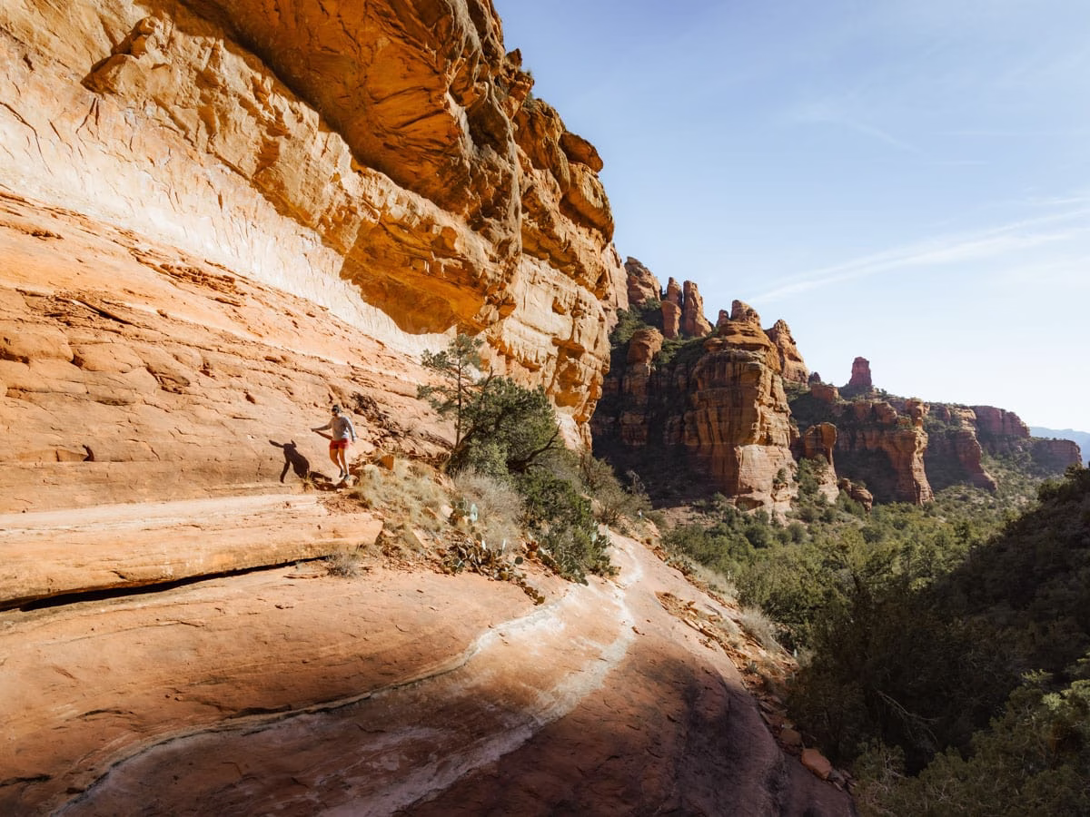Woman hiking on the slick red rock on the side of Fay Canyon walls in Sedona, Arizona.