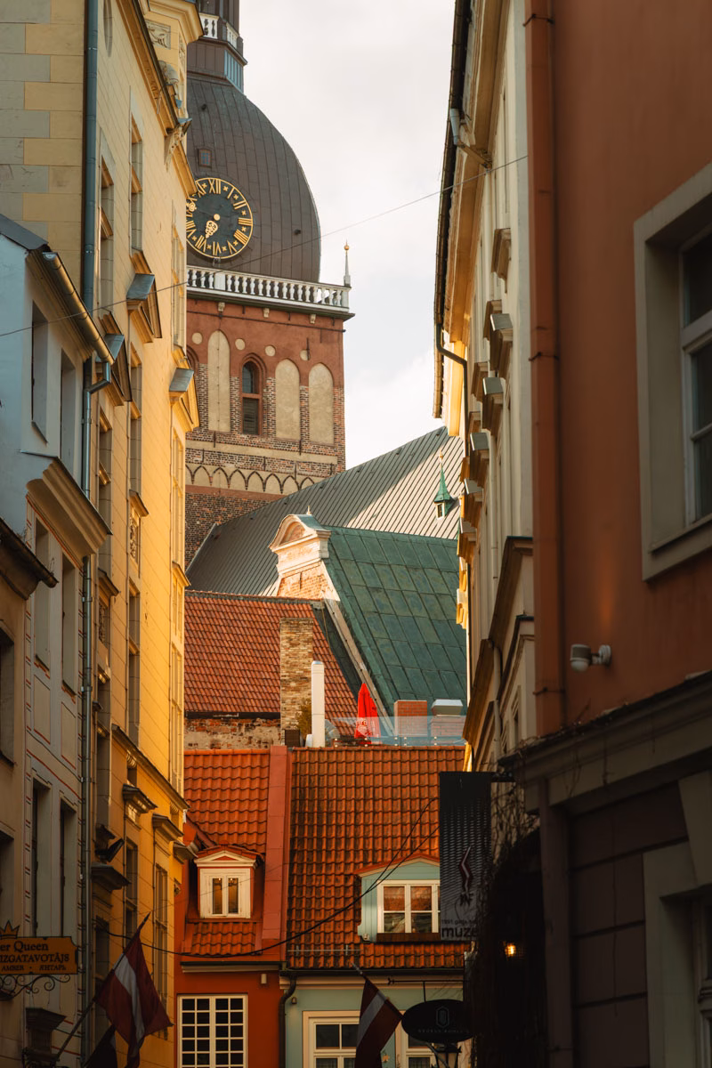 Narrow alley between historic buildings with a church clock tower visible in Riga's Old Town